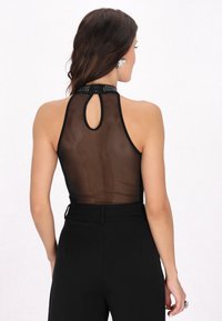 Body din plasă neagră cu gât înalt, detaliu cu spate în formă de cheiță și guler cu studuri. Asortat cu pantaloni negri cu talie înaltă pentru un aspect elegant.