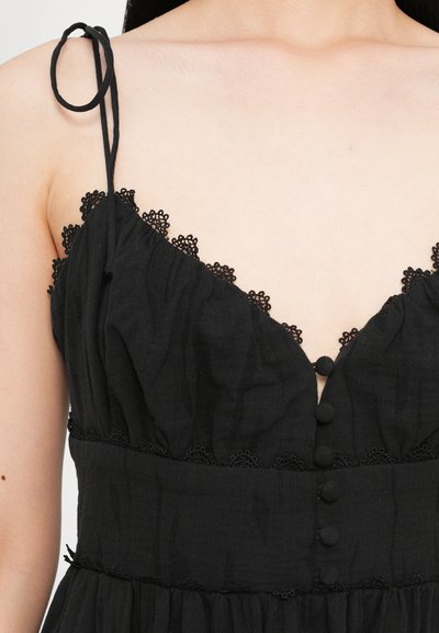 Schwarzes Kleid mit Spitzeneinsätzen am Ausschnitt, verstellbaren Spaghettiträgern und Stoffknöpfen auf der Vorderseite. Weiches, strukturiertes Material.