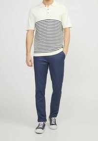 Men's short-sleeve polo shirt in cream with navy horizontal stripes, paired with navy pants and black sneakers. Classic collar and buttons.