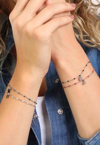 Drie delicate armbanden van zilver, versierd met kleurrijke kralen in zwart, rood en turquoise, met kleine geometrische bedels en een soepel kettingontwerp.