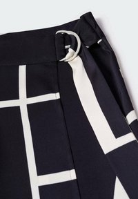 Tissu à carreaux noir et blanc avec fermeture à boucle en D en métal argenté, mettant l'accent sur la zone de la taille d'un vêtement.