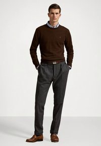 Brun tröja, ljusblå skjorta med krage, grå tweedbyxor och bruna läderskor. Tröjan har rund halsringning; byxorna har veck.