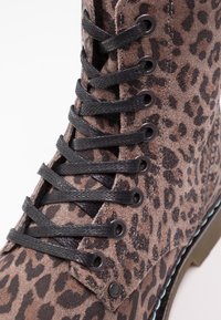 Botte en daim marron avec imprimé léopard noir, lacets noirs passant par des œillets en métal, et couture visible le long du côté.