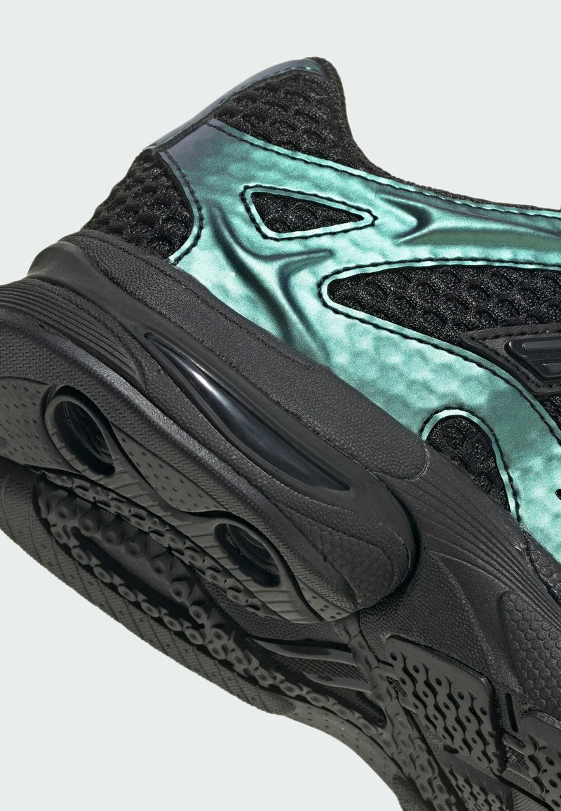 Close-up af sort sneaker med tekstureret sål og skinnende turkis syntetiske paneler over sort mesh-overdel.