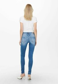 Jeans ajustados en azul hechos de denim, con un lavado medio, bolsillos traseros y una cintura alta, combinados con una camiseta blanca y sandalias.