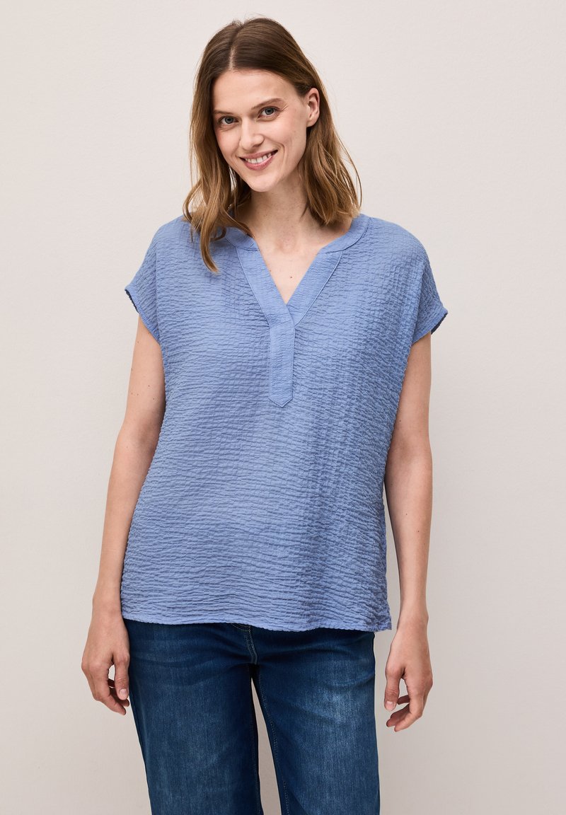 Top corto a maniche corte di un azzurro chiaro, con scollatura a V e vestibilità rilassata, abbinato a pantaloni in denim. Materiale morbido e dettagli di design discreti.