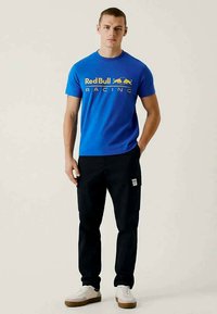 Sinine puuvillane T-särk, millel on kollane "Red Bull Racing" logo, koos mustade cargo-pükstega ja valgete spordijalatsitega, millel on pruunid tallad.