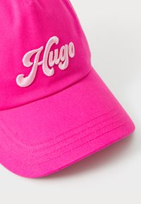 Rózsaszín baseball sapka pamutból, ívelt napellenzővel. Elöl hímzett "Hugo" felirat fehér színben. Textúrált anyag.