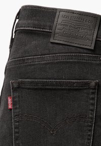 Jeans de mezclilla negra con una etiqueta de cuero que dice "Levi Strauss & Co." y una etiqueta roja en el bolsillo. Presenta costuras curvas en el bolsillo trasero.