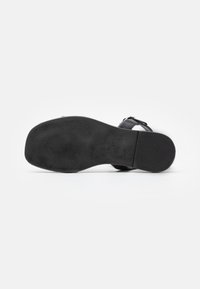 Sandale noire avec une tige en cuir lisse, une sangle de cheville ajustable et une semelle en caoutchouc texturée. Dispose d'une semelle intérieure ergonomique pour le confort.