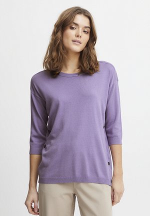 Lavendel trui met driekwart mouwen, ronde hals, zijknopen en een zachte textuur, gecombineerd met beige broek.