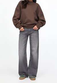 Brun oversized sweatshirt kombineret med grå vidde bukser. Outfittet inkluderer grønne sneakers med brune såler. Ensartede teksturer, afslappet design.