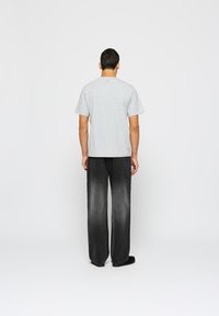 Pelēka kokvilnas t-krekla īsām piedurknēm attēlotā no aizmugures, apvienota ar brīviem melnām džinsu biksēm. Vienkāršs dizains, nav redzamu rakstu vai logo.