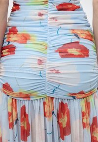 Φόρεμα ανοιχτού γαλάζιου χρώματος με ρυτιδωτή υφή, μεγάλο κόκκινο, πορτοκαλί και κίτρινο λουλουδάτο σχέδιο και λεπτομέρειες με συγκεντρωμένο ύφασμα στη μέση και την φούστα.