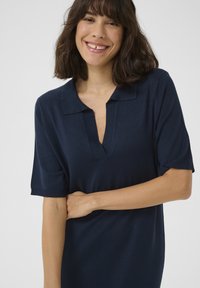 Abito polo corto navy a maniche corte con scollo a V profondo e polsini a coste, realizzato in un tessuto morbido che si adatta delicatamente al corpo.