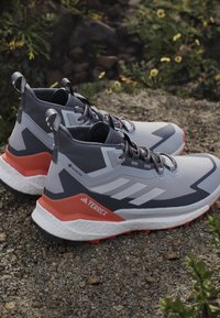 Szare i białe półwysokie buty sportowe z czerwonymi akcentami, z teksturowaną cholewką, sznurówkami i wzorzystą podeszwą. Zawiera wbudowaną metkę.