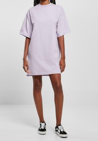 Liliowa, oversize sukienka t-shirt, krótki rękaw, okrągły dekolt, miękka bawełniana tkanina, proste wykończenie, w zestawieniu z czarno-białymi trampkami.