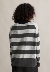 Pull rayé aux couleurs grises et noires, fabriqué en matière tricotée douce. Présente un col rond et des manches longues avec des bords côtelés.