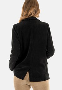 Blazer de pana negra con mangas largas, solapa con muesca y aberturas laterales, que muestra una superficie texturizada y un corte a medida.