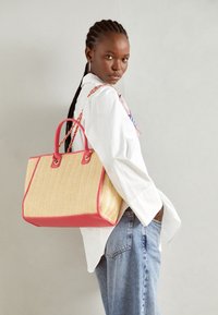 Spleciona torba na ramię z siana z różowymi skórzanymi akcentami i uchwytami. Posiada wzór w jodełkę oraz uporządkowany prostokątny kształt.