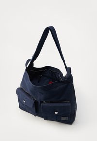 Sac fourre-tout en toile marine avec une large ouverture, deux poches zippées à l'avant et une poche intérieure supplémentaire. Il est doté d'une bandoulière robuste et d'un tissu texturé.
