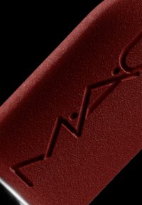 Un tubo di rossetto di un profondo bordeaux presenta una superficie opaca testurizzata con un logo impresso. La sezione inferiore è di un nero lucido.