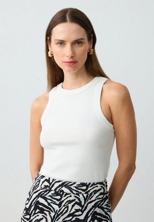 Weißes ärmelloses Oberteil mit rundem Ausschnitt, taillierter Passform und glatter Textur. Kombiniert mit einem gemusterten blau-schwarzen Zebra-Print-Rock.