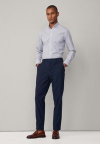 Gestreepte overhemdd blouse in lichtblauw en wit, gecombineerd met donkerblauwe tapered broek en bruine nette schoenen. Eenvoudig ontwerp,tailleerpasvorm.