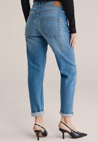 Svetlomodré rifle z denimu s voľným strihom, zavinutými manžetami, dvoma zadnými vreckami a hnedou koženou značkovou záplatou na páse.