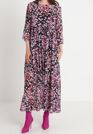 Robe maxi noire à fleurs, avec des manches trois quarts, ornée de fleurs roses et blanches et dotée d'une taille cintrée. Associée à des talons aiguilles roses.