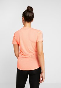 Helder koraalkleurig t-shirt met korte mouwen, ronde hals, een gladde textuur en een getailleerde pasvorm, gecombineerd met zwarte legging.