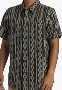 Camisa de manga corta en negro y crema, con un patrón geométrico de triángulos, cierre de botones y un bolsillo en el lado izquierdo del pecho.