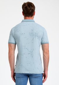 Gaiši zila polo krekls ar teksturētu rakstu, tumšākas zilas akcentiem un kontrastējošu apdari apkaklītē. Iekļautas īsās piedurknes.