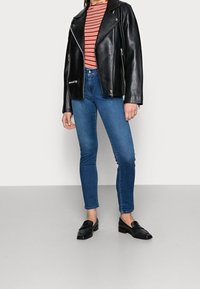 Svart läderbikerjacka, röd och vit randig topp, blå tajta jeans och svarta loafers. Fokusera på materialet och den åtsittande designen.