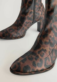 Bottes à talons hauts en imprimé léopard avec un design épuré, fabriquées en tissu, comportant un orteil pointu et une texture lisse. Accents noirs partout.