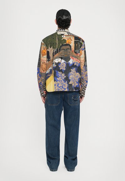Bunt gestreifte Jacke mit künstlerischen Drucken, langen Ärmeln und lockerer Passform. Kombiniert mit locker sitzenden, dunkelblauen Jeans.