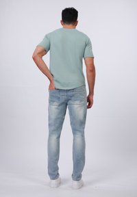 Camiseta de manga corta verde claro, combinada con jeans desgastados de mezclilla azul claro y zapatillas blancas, vista desde la espalda. Ajuste casual y diseño sencillo.