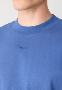Blue cotton t-shirt with a crew neckline. Features stitched logo "HUGO" in darker blue on the chest. Smooth texture, relaxed fit.