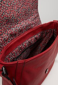Červená kožená kabelka s květovanou textilní podšívkou, vybavená zapínacím kapsou na zip, stříbrným kováním a magnetickým uzávěrem.