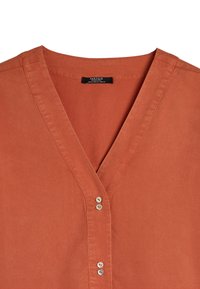 Rdzawa bluzka z dekoltem w serek, zapinana na cztery guziki, wykonana z gładkiego materiału. Metka wszyta w dekolt.