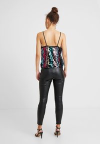 Paljetterad ärmlös topp med flerfärgade mönster och svart kant, kombinerad med svarta åtsittande läderbyxor och svarta remsandaler.
