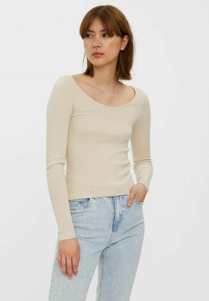 Maglia a maniche lunghe beige a coste con scollatura a girocollo, vestibilità slim e texture morbida, abbinata a jeans in denim azzurro chiaro.