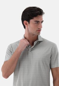 Helles graues Polohemd mit einem dezenten geometrischen Muster, einer Knopfleiste mit drei Knöpfen und einer weichen Textur. Kurze Ärmel und flexibles Kragen-Design.