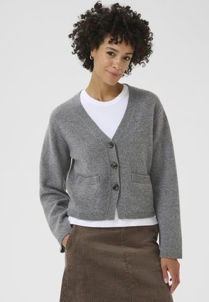Gray knitted cardigan with a V-neck, button closure, and two front pockets, paired with a white shirt and brown corduroy skirt.