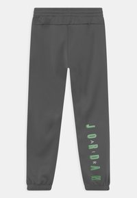 Ciemnoszare spodnie sportowe z elastycznym pasem i mankietami, z pionowym napisem "JORDAN" w zielonym i białym na prawej nodze.