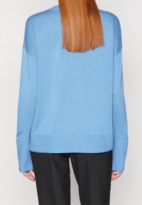 Blauer Strickpullover mit lockerer Passform, mit überschnittenen Schultern, gerippten Bündchen und Saum sowie einer weichen Textur. Getragen mit schwarzen Hosen.