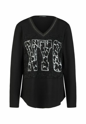 Schwarzes Langarm-V-Ausschnitt-Shirt mit Spitzeneinsatz und großen weißen gemusterten "NYC" Buchstaben vorne.