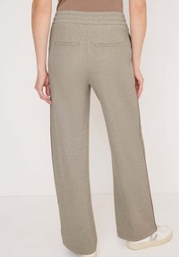 Pantalons larges beige clair avec une texture douce, dotés d'une taille élastique, de deux poches arrière et de rayures latérales contrastantes.