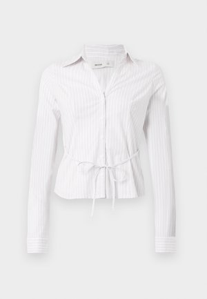 Λευκό πουκάμισο με μακριά μανίκια και ανοιχτόχρωμες κάθετες ρίγες, κλείσιμο με κουμπιά και λεπτομέρεια ζώνης στη μέση. Ύφασμα τραγανό με γιακά και μανίκια με μανσέτες.