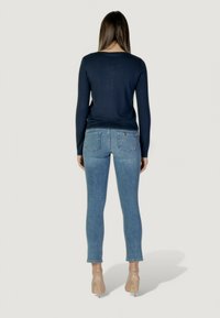 Pull en maille à manches longues de couleur marine avec un ourlet côtelé associé à un jean skinny bleu clair. Des talons transparents complètent la tenue vue de dos.